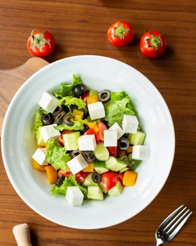 Greek salad in the white plate with tomatoes from top