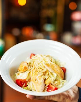 Man holding Caesar salad in the white plate with tomatoes from top