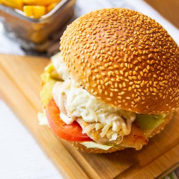 Caesar burger with french fries on the wood plate close up