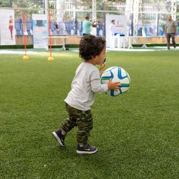 Baby boy running in the stadium with soccer ball