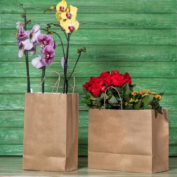 Beautiful colorful orchid, begonia, gardenia in the shopping bag with green background