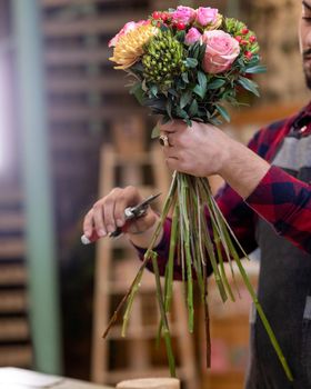 Florist man making flower bouquet, cutting flower at the store