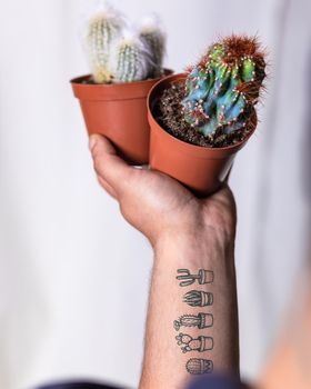 Man holding colorful cactuses with tattoo on hand