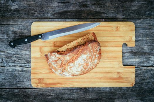Fresh dark bread in slices. Wooden cutting board and table, knife.