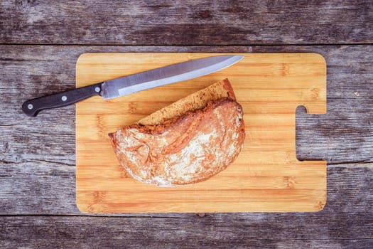 Fresh dark bread in slices. Wooden cutting board and table, knife.