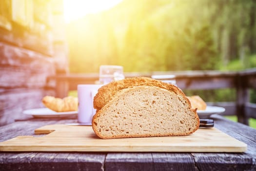 Fresh dark crisp bread for breakfast on an alpine hut. Wooden cutting board and milk in glass bottle. Sunshine.