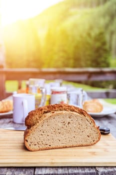 Fresh dark crisp bread for breakfast on an alpine hut. Wooden cutting board and milk in glass bottle. Sunshine.