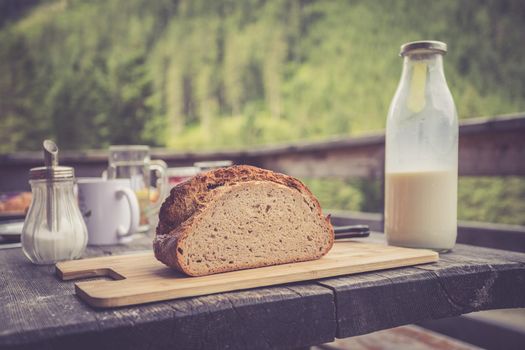 Fresh dark crisp bread for breakfast on an alpine hut. Wooden cutting board and milk in glass bottle.