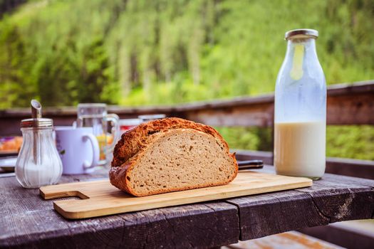 Fresh dark crisp bread for breakfast on an alpine hut. Wooden cutting board and milk in glass bottle.