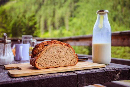 Fresh dark crisp bread for breakfast on an alpine hut. Wooden cutting board and milk in glass bottle.