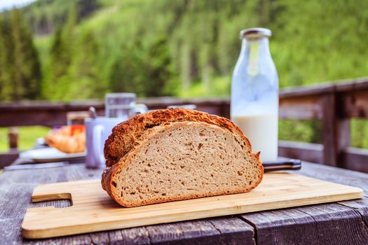 Fresh dark crisp bread for breakfast on an alpine hut. Wooden cutting board and milk in glass bottle.