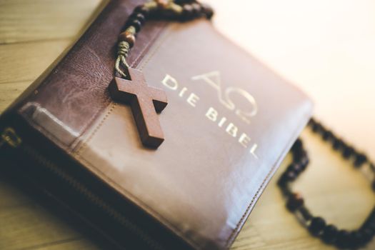 Holy bible and rosary are lying on a wooden desk