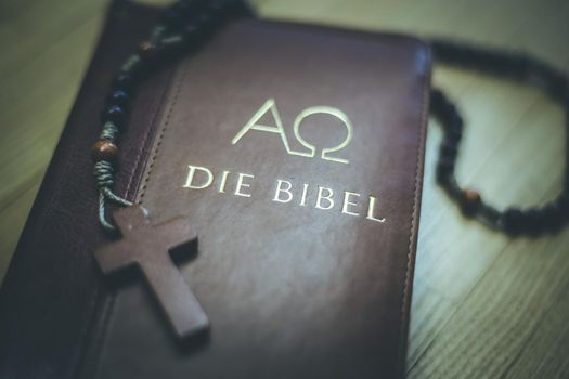 Holy bible and rosary are lying on a wooden desk