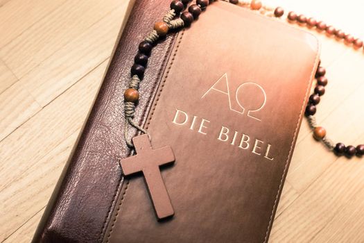 Holy bible and rosary are lying on a wooden desk