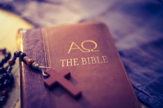 Holy bible and rosary are lying on a wooden desk
