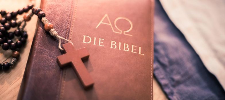 Holy bible and rosary are lying on a wooden desk