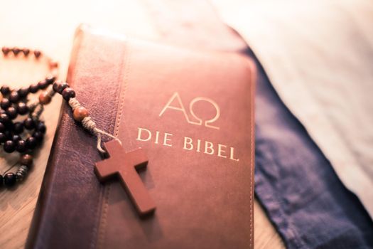 Holy bible and rosary are lying on a wooden desk