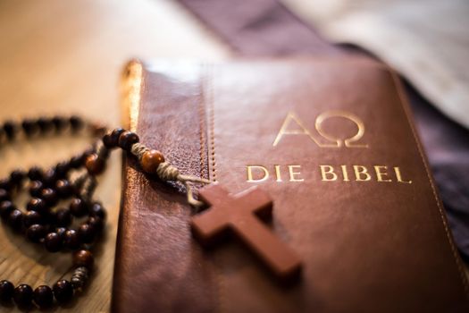 Holy bible and rosary are lying on a wooden desk