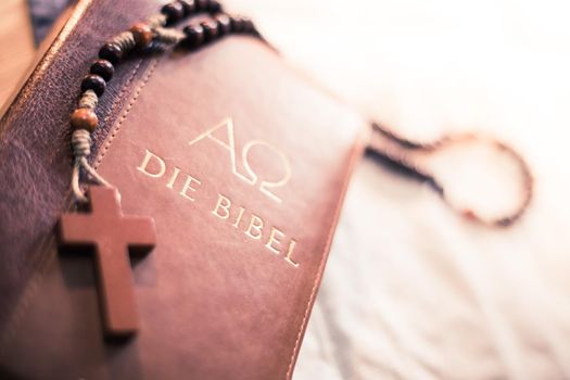Holy bible and rosary are lying on a wooden desk