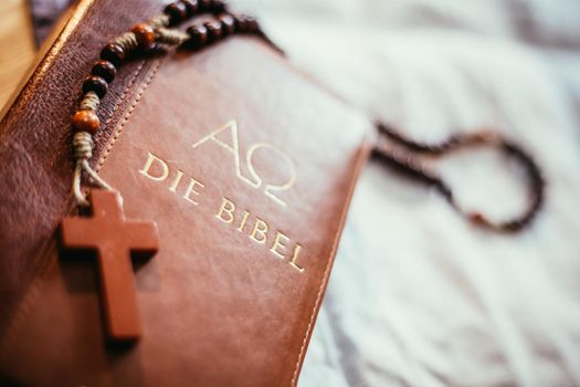 Holy bible and rosary are lying on a wooden desk