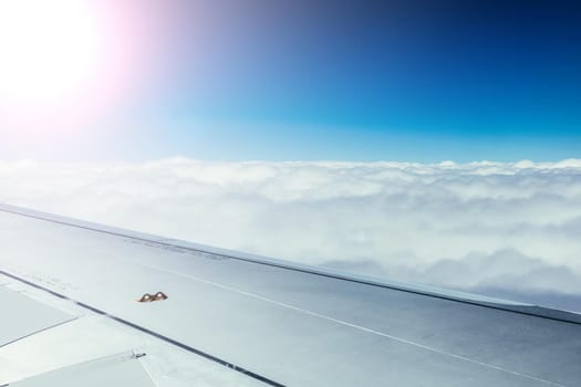 View of a grey airplane wing through the aircraft window. Sunshine, global warming.