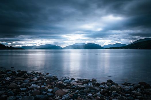 Beautiful mystic landscape lake scenery in Scotland with cloudy sky and sunbeams