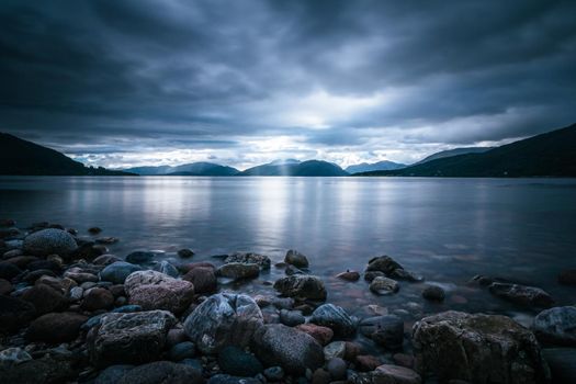 Beautiful mystic landscape lake scenery in Scotland with cloudy sky and sunbeams