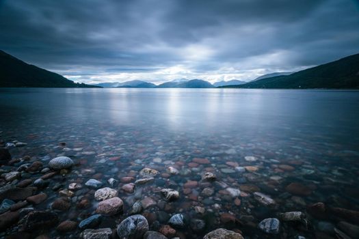 Beautiful mystic landscape lake scenery in Scotland with cloudy sky and sunbeams