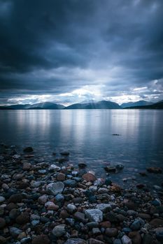 Beautiful mystic landscape lake scenery in Scotland with cloudy sky and sunbeams