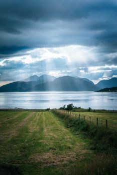 Beautiful mystic landscape lake scenery in Scotland with cloudy sky, meadow, trees and sunbeams