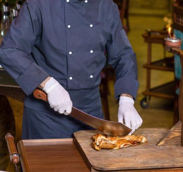 Chef cutting a chicken meat with a cleaver on the wood plate