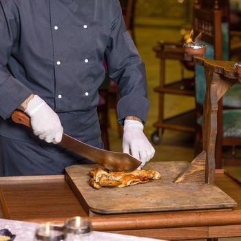 Chef cutting a chicken meat with a cleaver on the wood plate