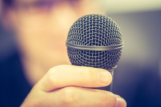 Microphone in the foreground, man taking into it in the blurry background