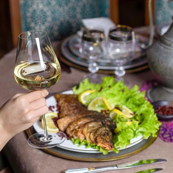 Woman eating a grilled whole fish with white wine