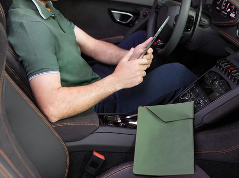 A young man with a tablet in his hand at the sports car. Multitasking