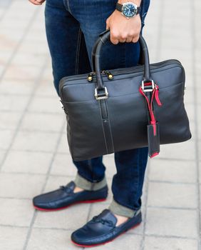 Young man holding a leather black handbag close up