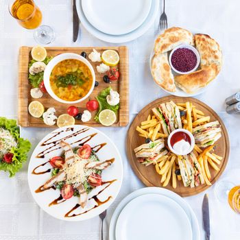 Club sandwich with french fries and soup, salad on the table, top view