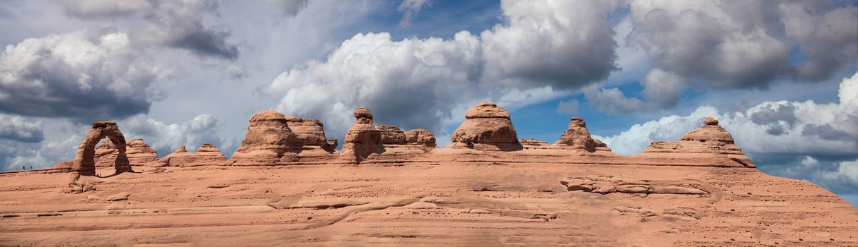 Delicate Arch panoramic view, Arches National Park. High resolution image of rock formations against blue sky.