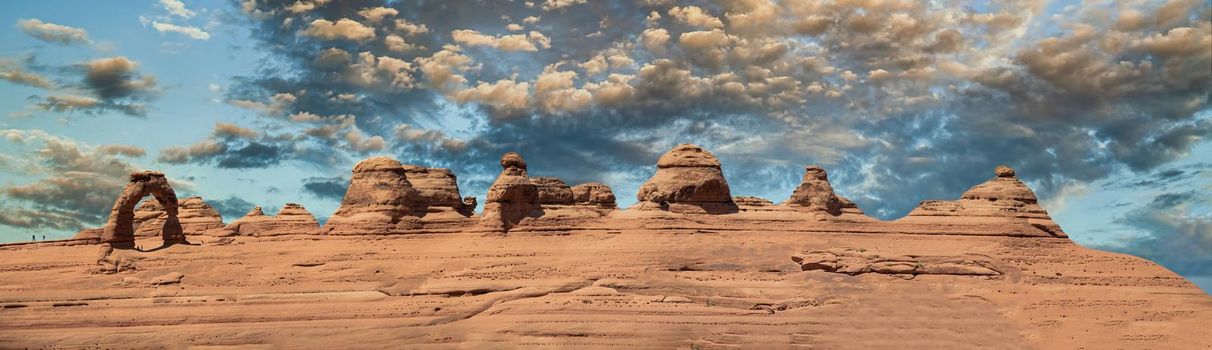 Delicate Arch panoramic view, Arches National Park. High resolution image of rock formations against blue sky.