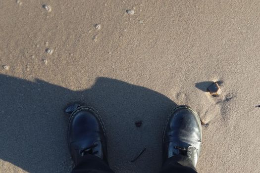 Human feet in black shoes at a baltic sea beach in northern Germany