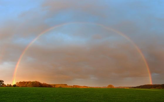 Evening landscape with rainbow and colored clouds