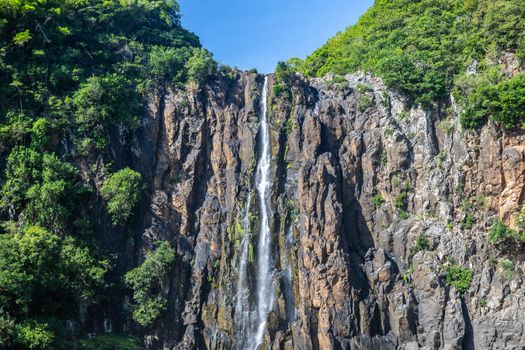 Rockface with waterfall Cascade Niagara at french island Reunion in the indian ocean on a sunny day with blue sky