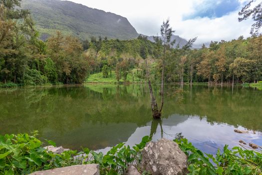 Landscape with idyllic lake, mountain range, green trees in the interior of the island Reunion in the indian ocean 