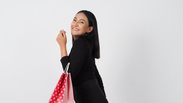 Sexy woman shopping. Portrait of excited beautiful girl wearing black holding red shopping bags isolated over white background. Cheerful happy lady enjoy carrying goods bags. half body.