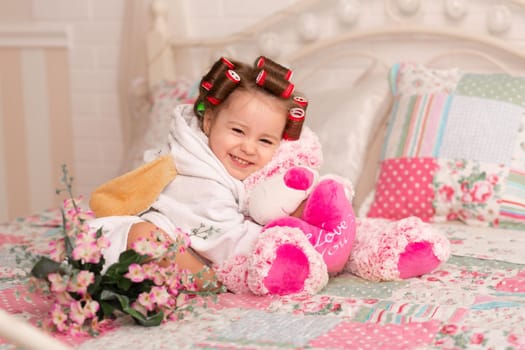 Adorable little girl with hair curlers hugs her favorite teddy bear toy.