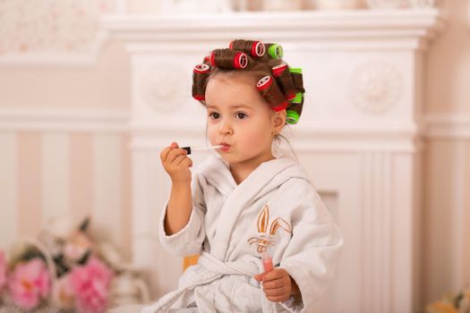 Adorable little girl with her mother in hair curlers apply makeup. Mom teaches daughter to use cosmetics. Beauty day. Girls are such girls.