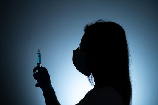 Young female doctor in a medical mask and gloves holds a syringe with a coronavirus vaccine and a vaccine chip inside. Conspiracy theory. Chipping people.