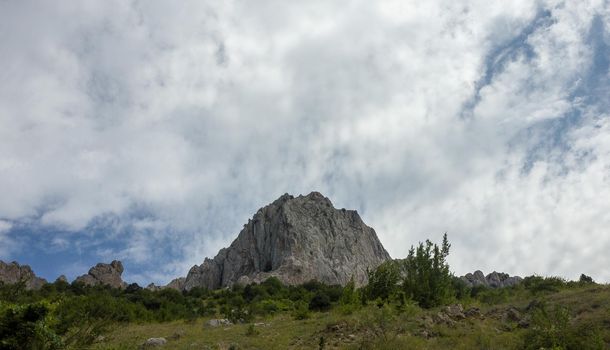Inaccessible rocks surrounded by green forests and shrubs in hot summers in clear sunny weather.