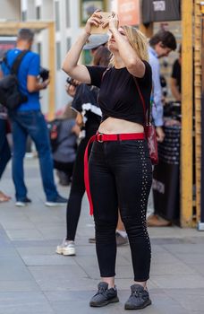 August 18, 2018. Moscow, Russia. A girl on a busy street photographs something interesting on her phone above.