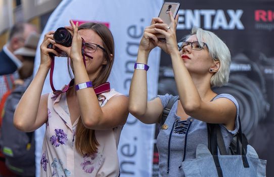 August 18, 2018. Moscow, Russia. Two girls on a busy street are taking pictures with their phones and cameras of something interesting above.
